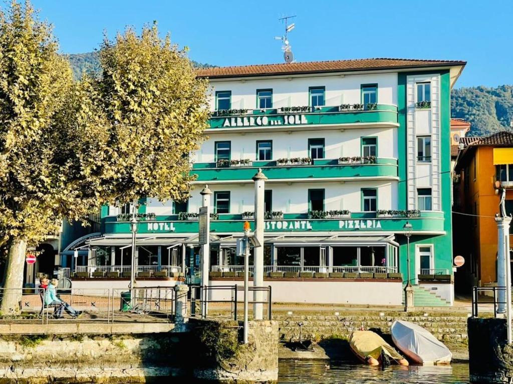 un grand bâtiment vert et blanc à côté d'une rivière dans l'établissement Albergo Del Sole, à Porto Valtravaglia