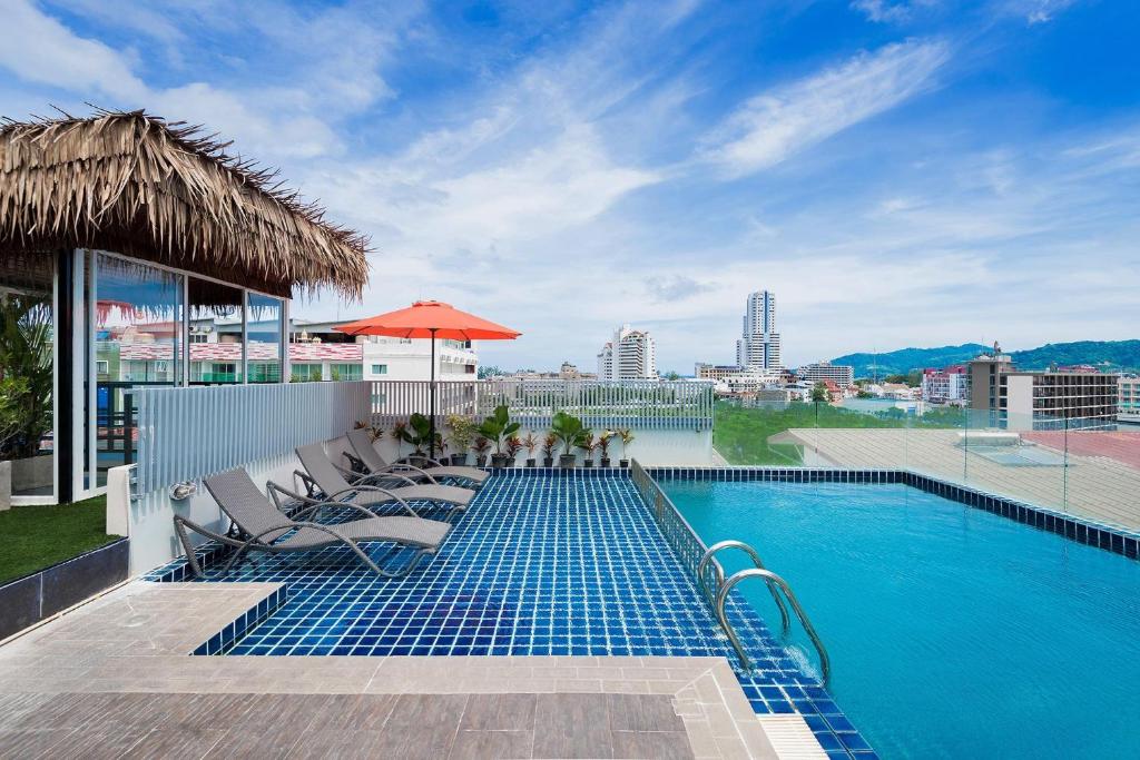 una piscina con sillas y una sombrilla en un edificio en Hallo Patong Hotel, en Patong Beach