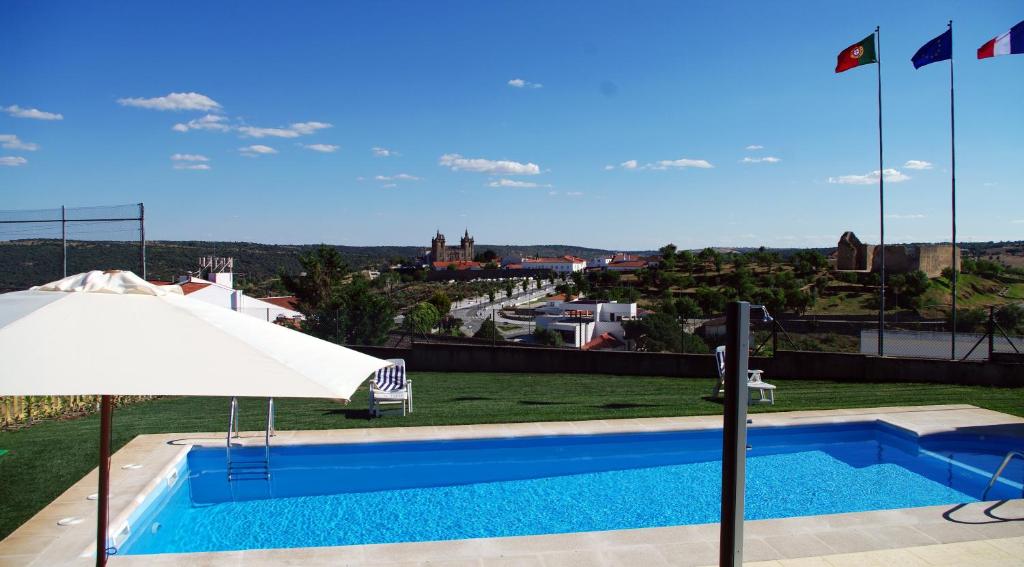 a pool with an umbrella and a view of a city at Hotel Cabeço do Forte in Miranda do Douro