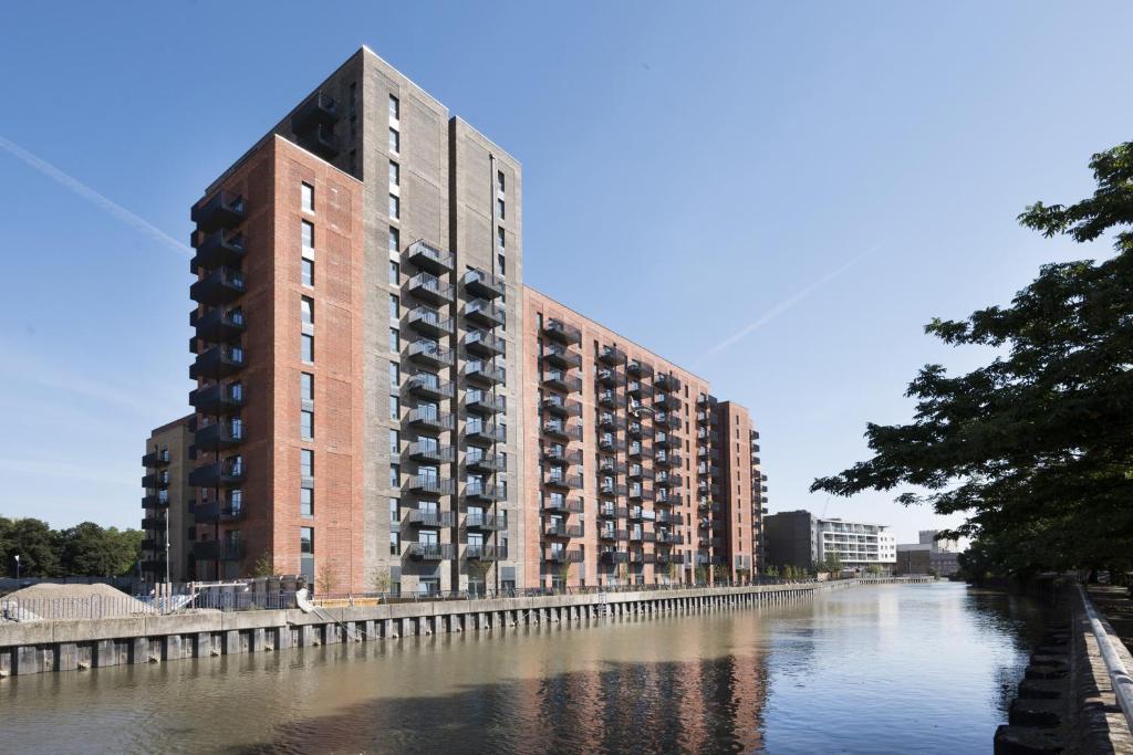 a large brick building next to a river at Modern Studios and Apartments at Barking Wharf in London in London