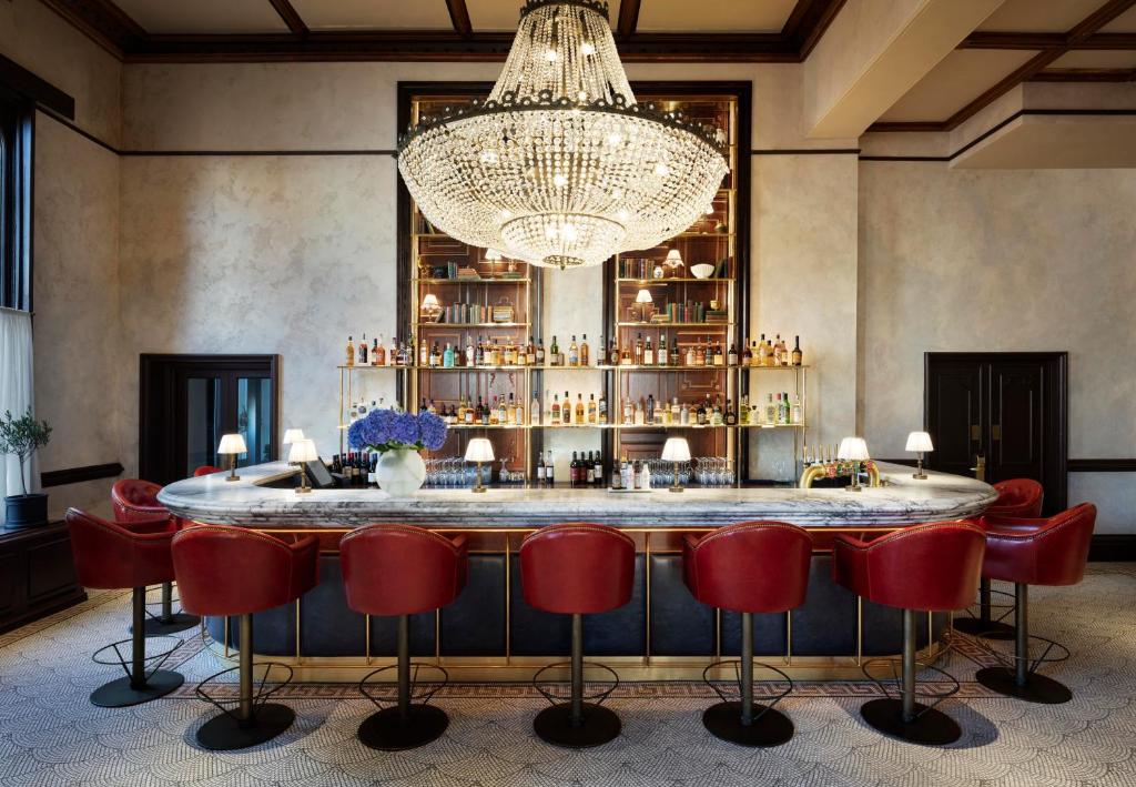 a bar with red chairs and a chandelier at The Randolph Hotel, by Graduate Hotels in Oxford