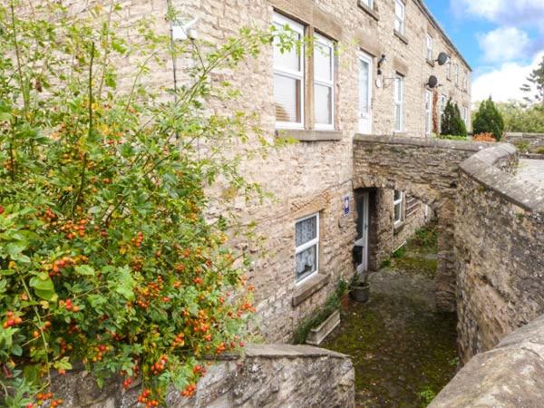 an old stone building with a bush in front of it at 2A Bridge Apartments in Masham