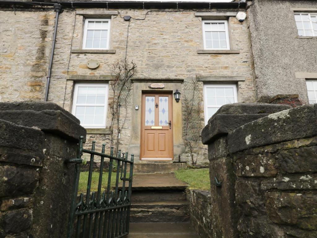 an old stone house with a orange door at Hope Cottage in Leyburn