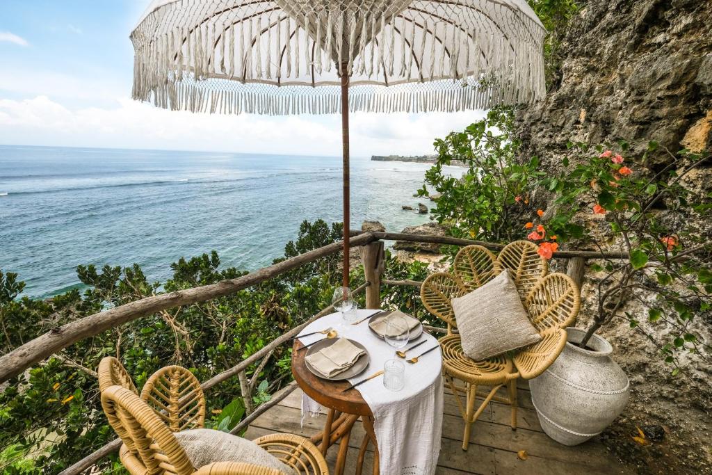 a table and chairs with an umbrella and the ocean at The Korowai in Uluwatu
