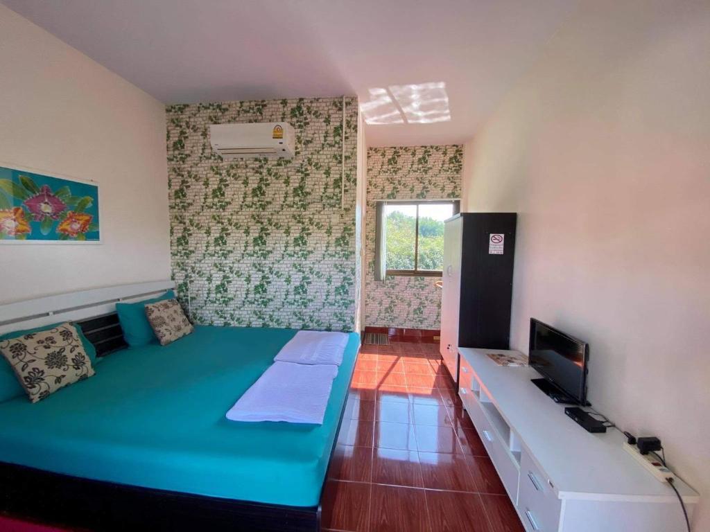 Habitación con cama verde grande y TV. en Saeng Tai Amphawa en Samut Songkhram