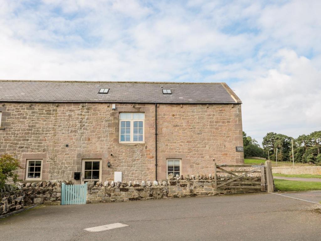 an old brick building with a fence in front of it at Watermill Cottage in Chathill