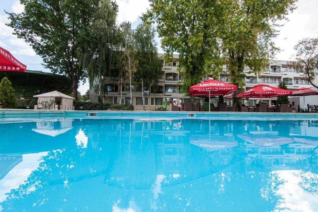 ネプトゥンにあるCocor Spa Hotelの青い水と赤い傘が備わるスイミングプール