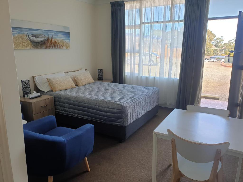 アラダラにあるサンドパイパー モーテル ウラデュラのベッドルーム1室(ベッド1台、テーブル、青い椅子付)
