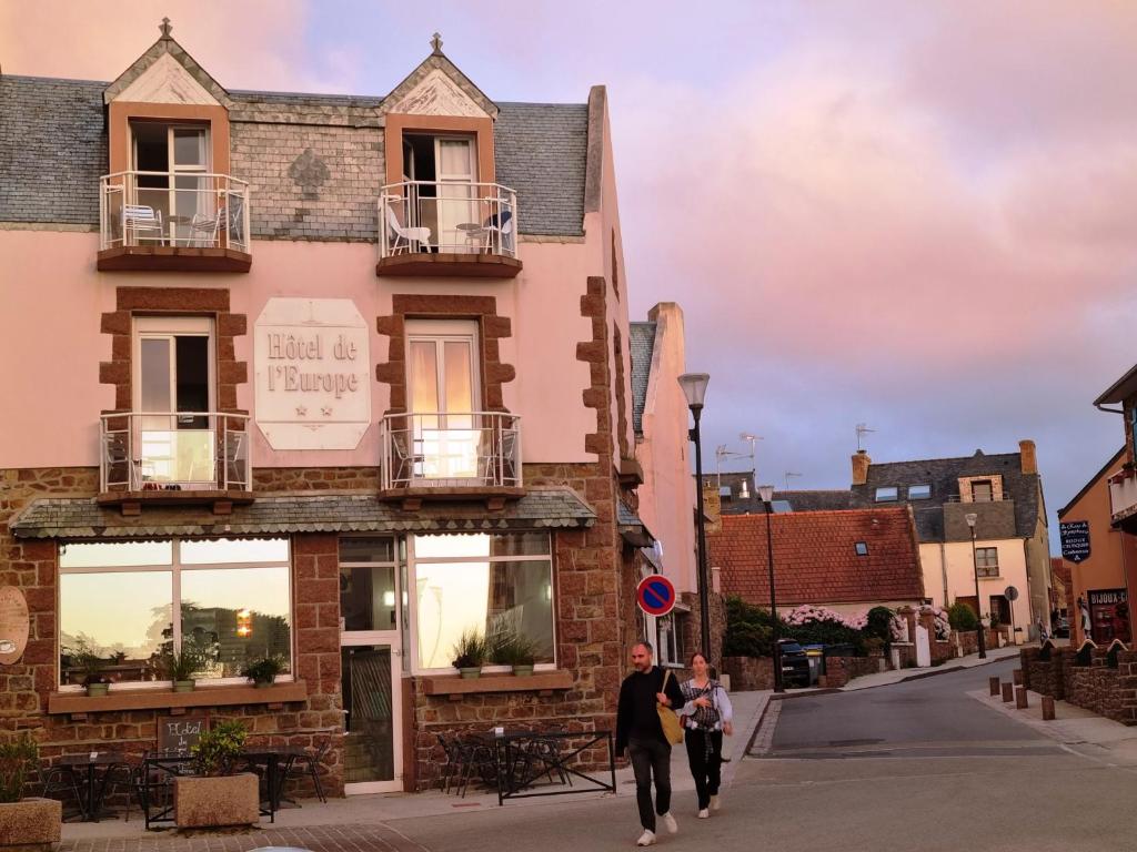 a man and a woman walking down a street in front of a building at Hotel De L'Europe in Perros-Guirec