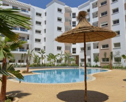 an umbrella and a swimming pool in front of a building at Good appartement near at the aeroport in Nouaseur