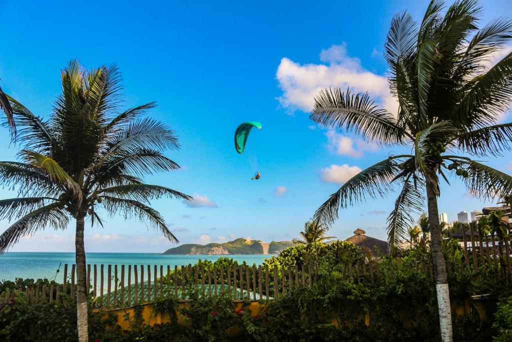 a person flying a kite over the ocean with palm trees at Atlântico Flat Natal in Natal