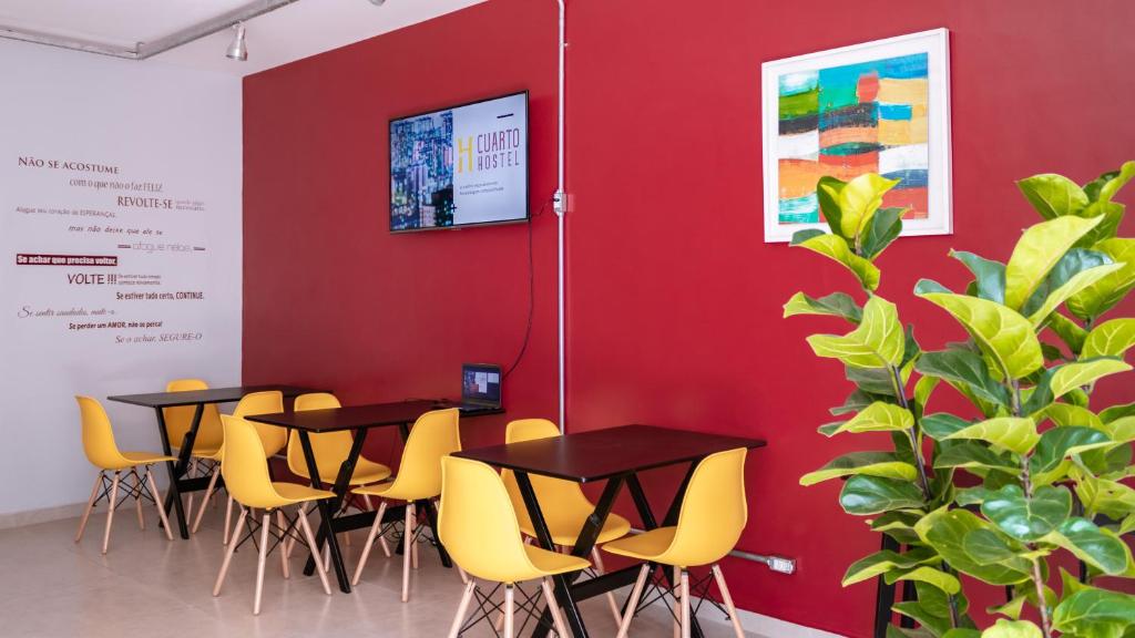 a row of tables against a red wall with yellow chairs at HOSTEL CUARTO in Sao Paulo