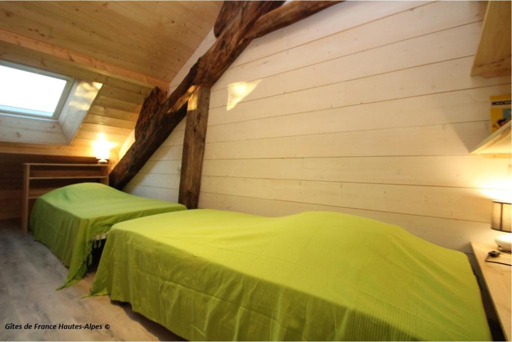 two green beds in a room with wooden walls at La Rawette in Puy-Sanières