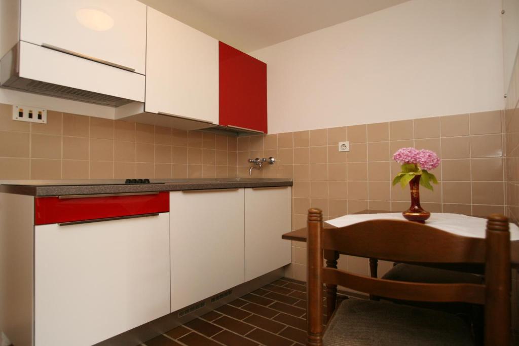 a kitchen with white cabinets and a table with a vase of flowers at Apartments Neda - Poreč South in Poreč