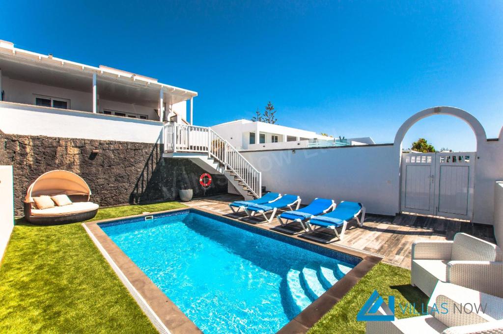 una piscina con sillas azules y una casa en Villa Graciosa By Villas Now Ltd, en Playa Blanca