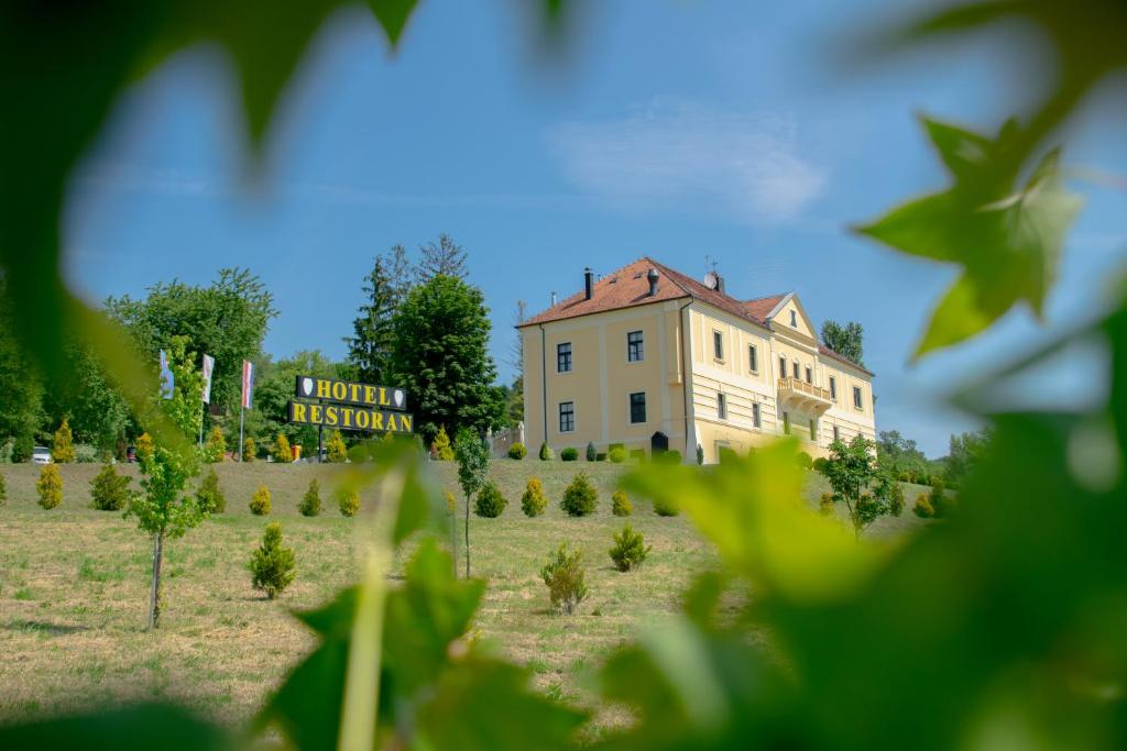 un edificio en un campo con un cartel delante en Hotel & Restoran Dvorac Gjalski en Zabok