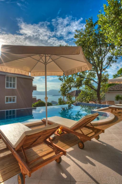 a wooden lounge chair with an umbrella next to a swimming pool at Harmonia Bungalows & Pool in Sveti Stefan