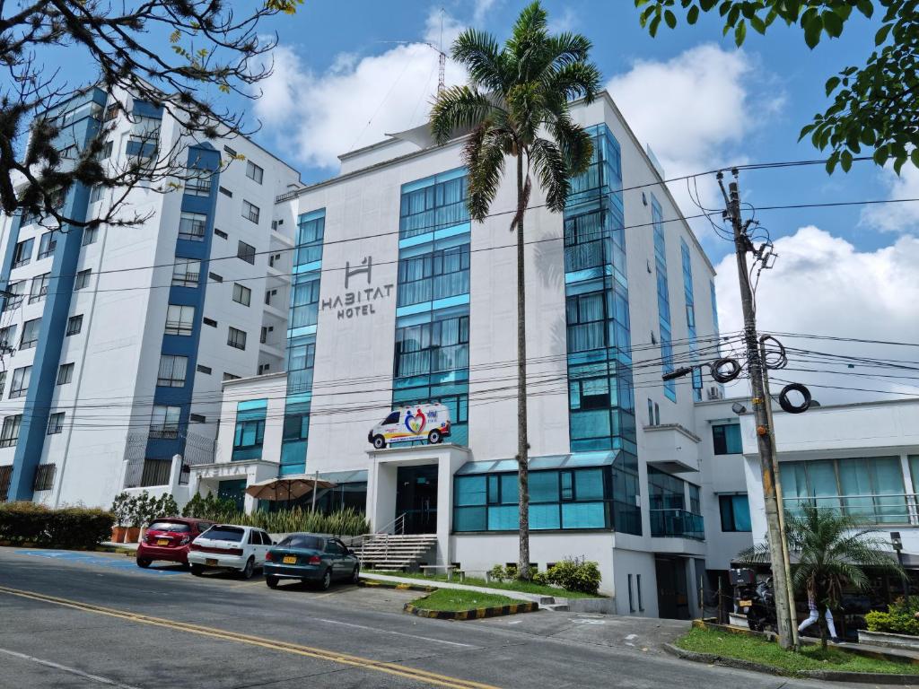 a building with a palm tree in front of a street at Habitat Suites Hotel in Pereira