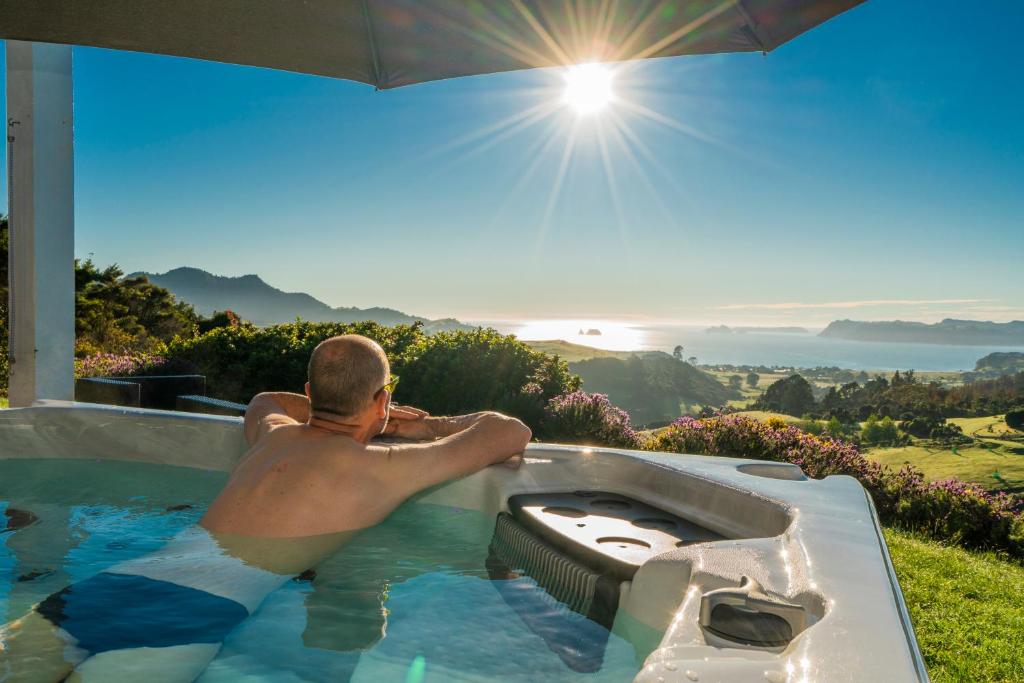 a man sitting in a hot tub in the sun at Bayview Valley Lodge Bed & Breakfast in Whitianga
