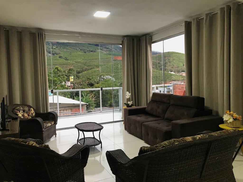 ein Wohnzimmer mit einem Sofa und Stühlen sowie einem großen Fenster in der Unterkunft Apartamento Fruto da Terra 301 VISTA PANORÂMICA MONTANHAS in Caparaó Velho