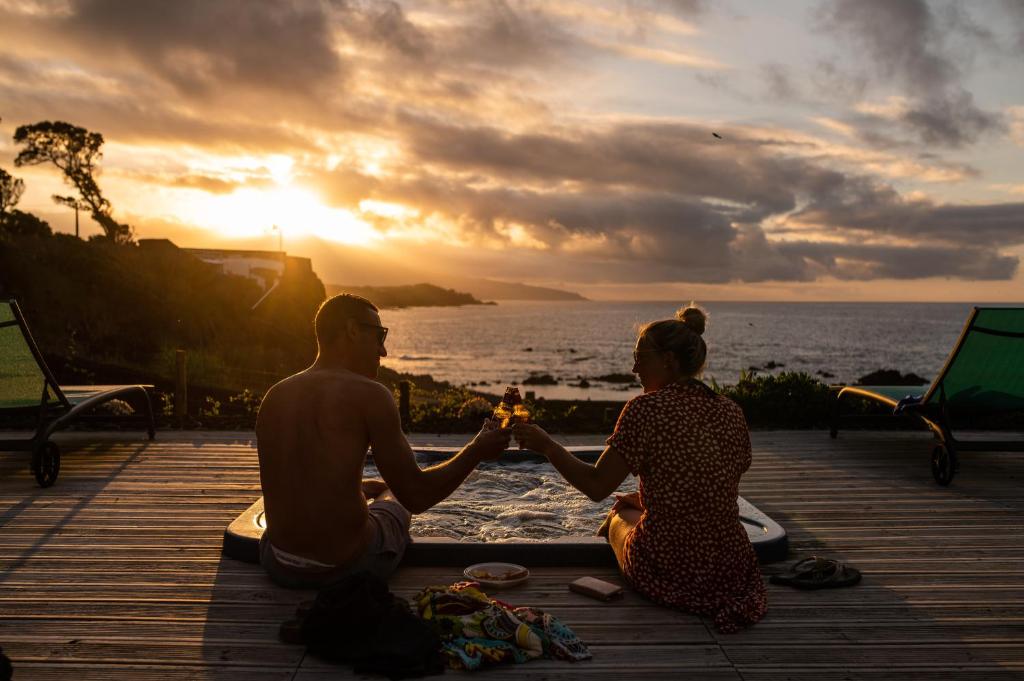 een man en een vrouw die op een steiger hand in hand zitten bij zonsondergang bij Azor'Oasis in Calhetas