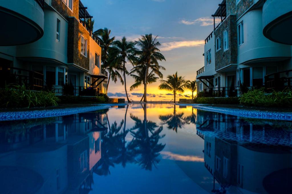 a resort pool with palm trees and a sunset at 7Stones Boracay in Boracay