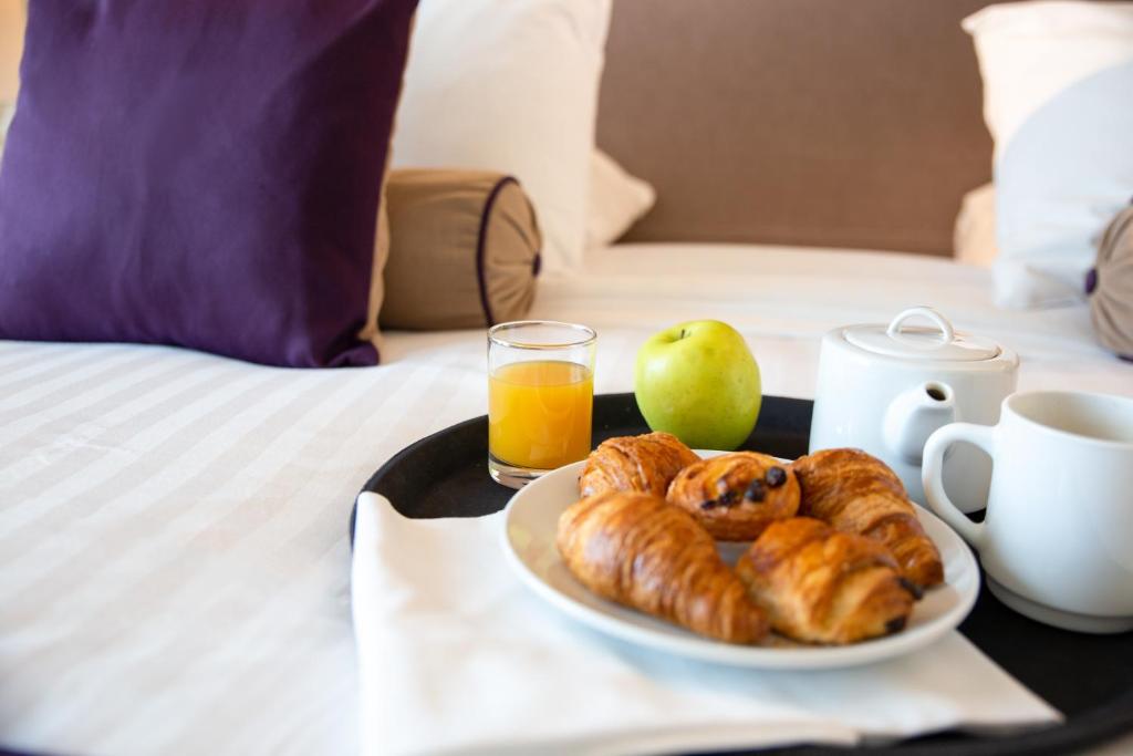 a tray with a plate of pastries and an apple on a bed at Zenitude Relais &amp; Spa - Paris Charles de Gaulle in Roissy-en-France
