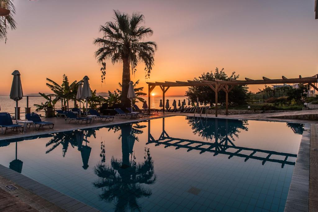 a swimming pool with a sunset in the background at Belussi Beach Hotel & Suites in Kipseli