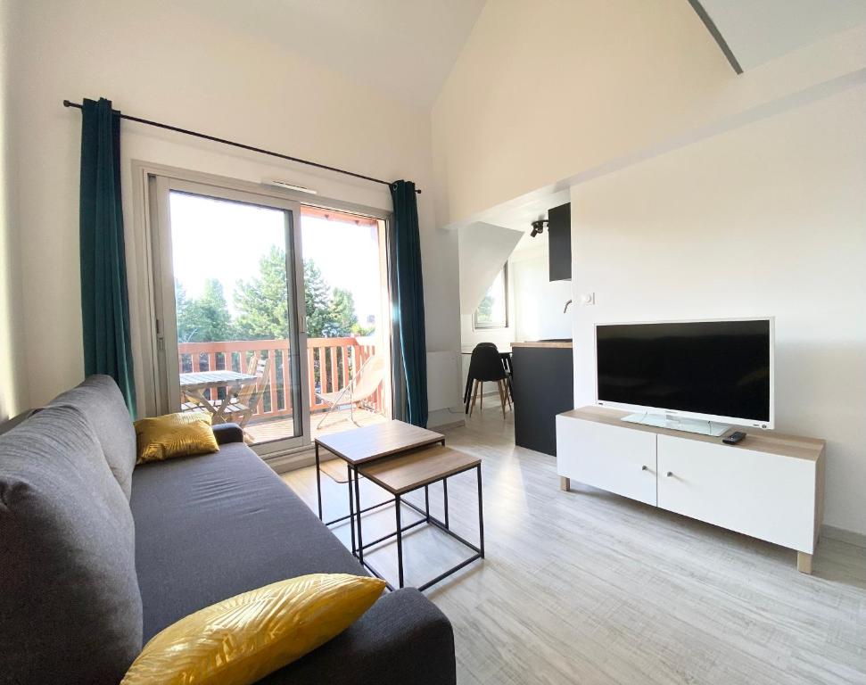 a living room with a couch and a flat screen tv at L'OREE DE DEAUVILLE, CHARMANT DUPLEX PROCHE PLAGE in Tourgeville