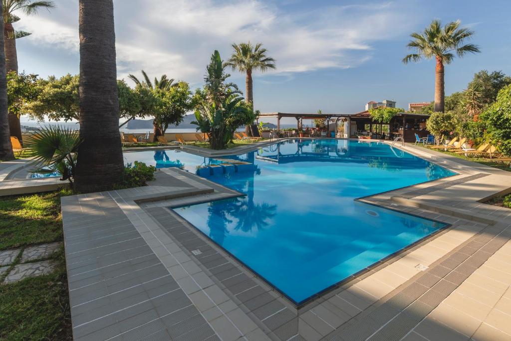 a pool with palm trees and blue water at Chrissida Hotel in Nea Kydonia