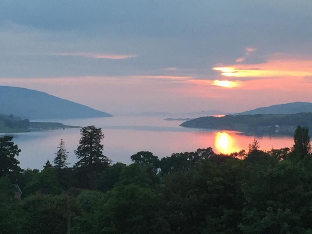 a sunset over a body of water with trees at Loch Broom Cabins Seaviews& Petfriendly in Leckmelm