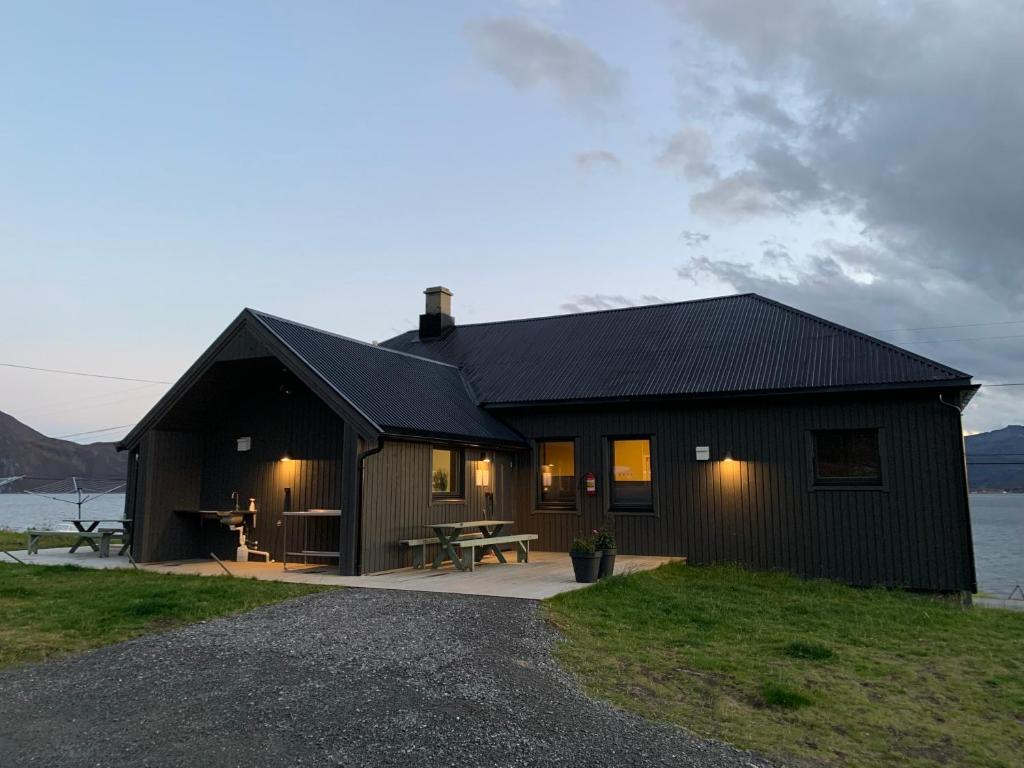 a black house with a picnic table next to a lake at BEDEHUSET Basecamp Senja in Skaland