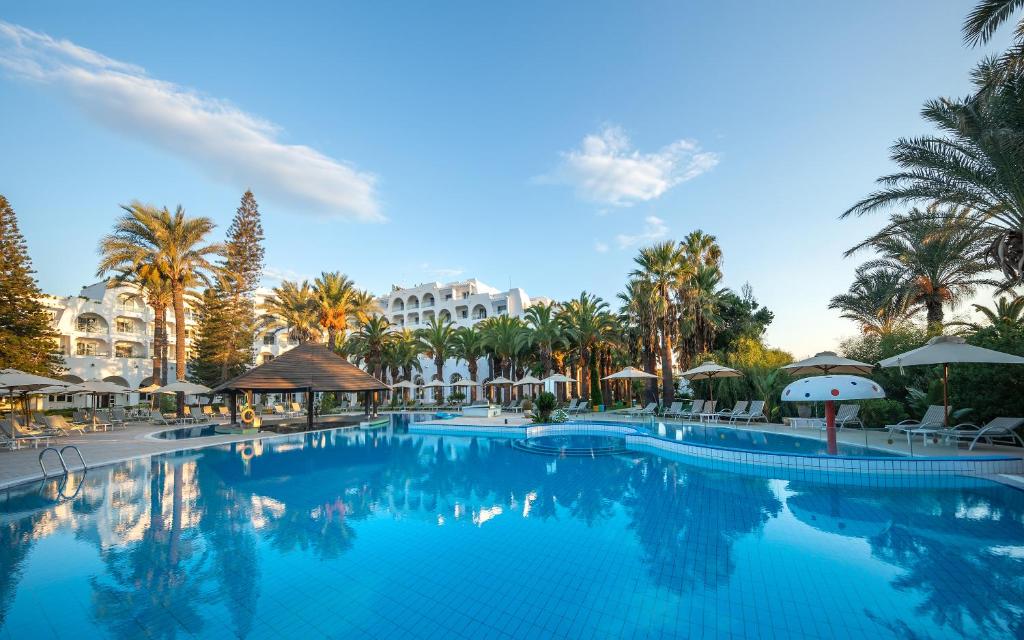 una piscina en el complejo con palmeras y sombrillas en Hotel Marhaba Beach, en Sousse