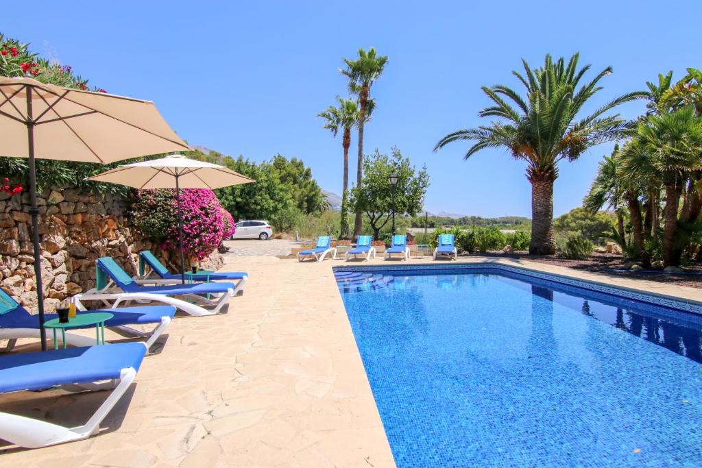 una piscina con sillas, sombrillas y palmeras en Villa Dulce Manchón en Altea