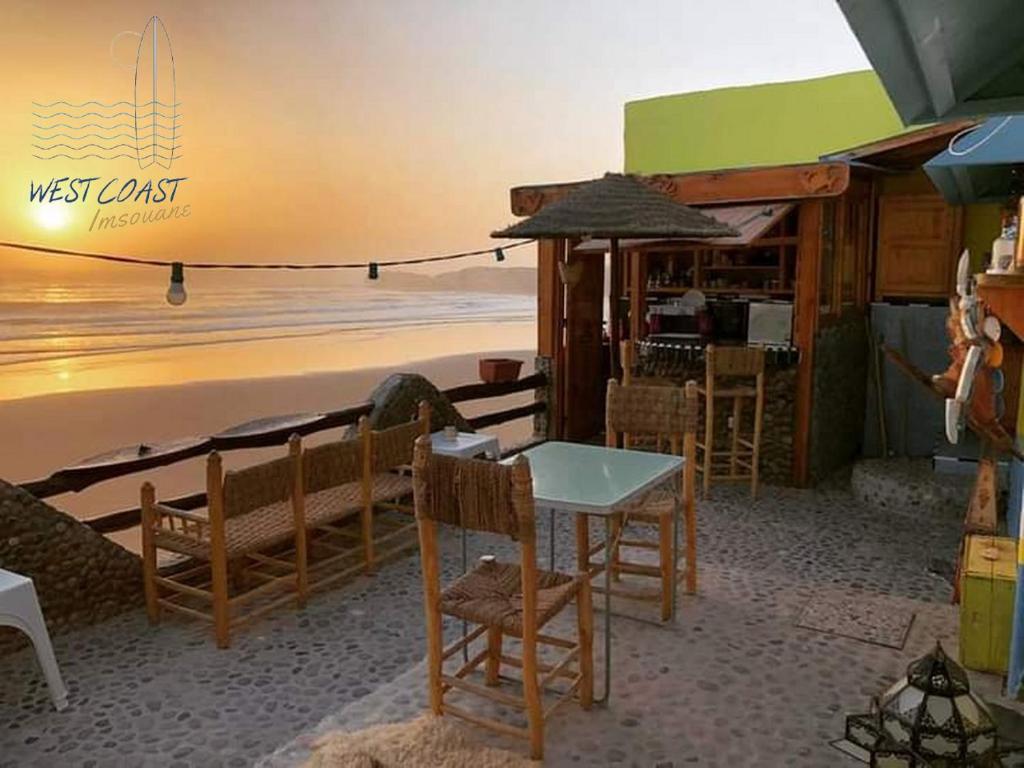 un ristorante sulla spiaggia con tavolo e sedie di WEST COAST HOSTEL a Imsouane