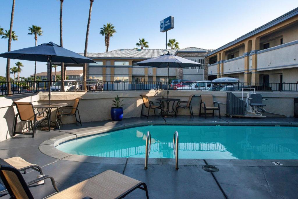 a swimming pool with tables and chairs and umbrellas at Best Western Kettleman City Inn & Suites in Kettleman City