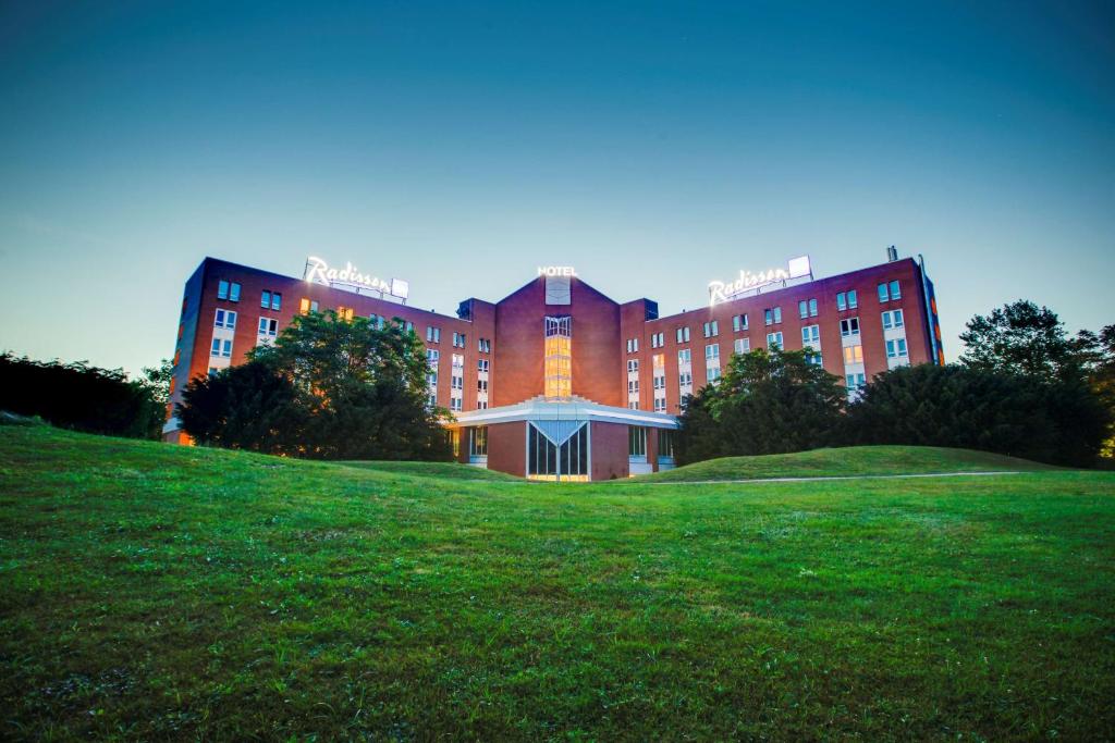 un grande edificio in mattoni rossi su una collina erbosa di Radisson Blu Hotel Karlsruhe a Ettlingen