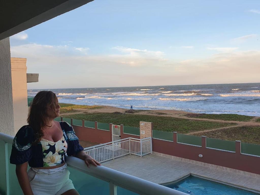 kobieta stojąca na balkonie patrząca na ocean w obiekcie Apartamento Vista Mar – Pé na Areia w mieście Cabo Frio