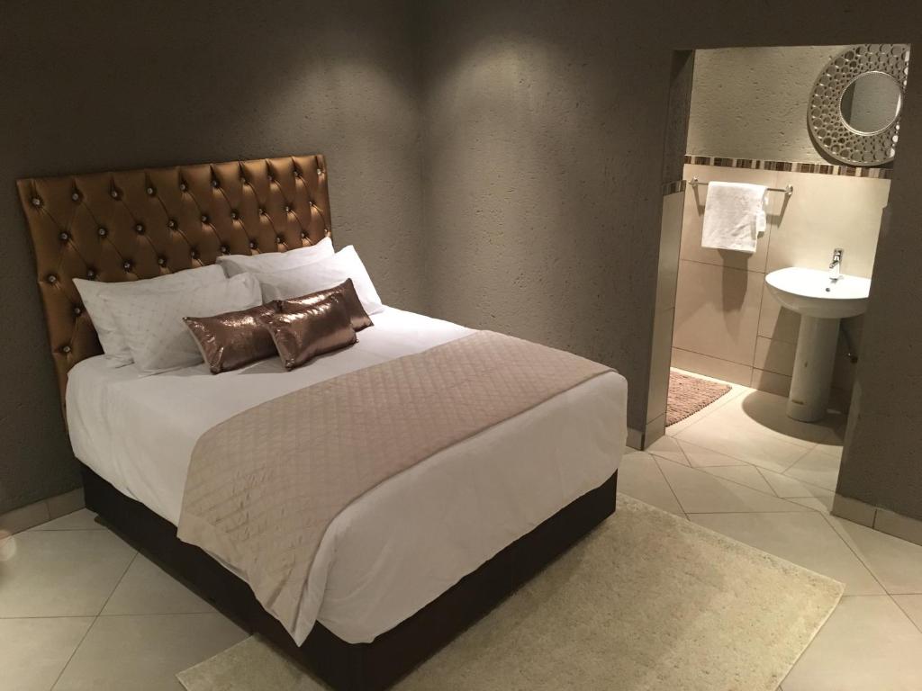 een slaapkamer met een bed en een badkamer met een wastafel bij Charli’s Lodge in Mpheleng