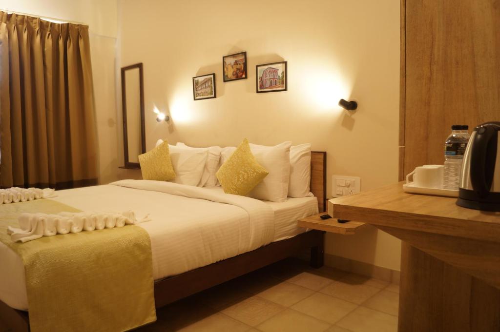 um quarto de hotel com uma cama com lençóis brancos e almofadas amarelas em Sharayu One em Mapuçá