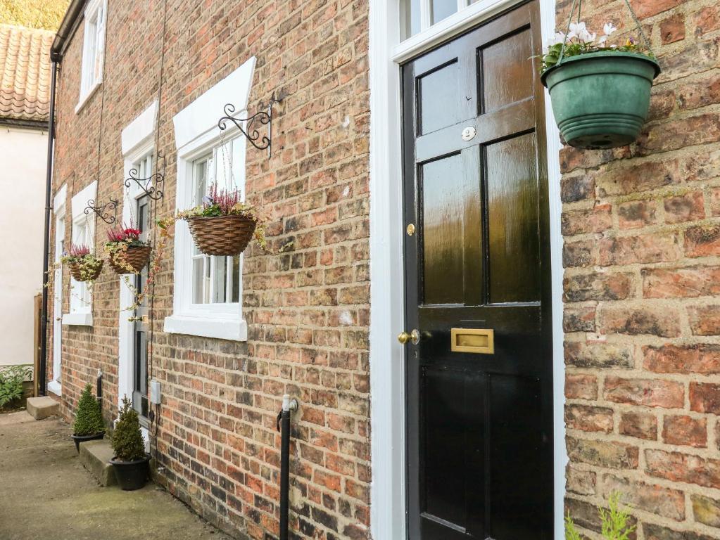 a brick house with a black door and potted plants at Court Cottage in Ripon