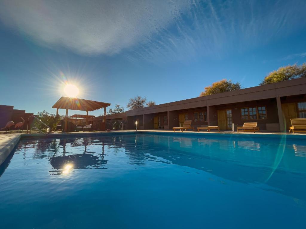 a large swimming pool with an umbrella and a building at Ittai Hotel in San Pedro de Atacama