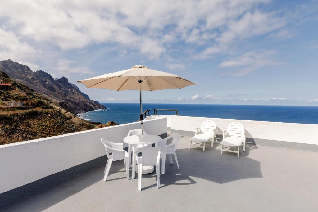 eine Terrasse mit weißen Stühlen, einem Sonnenschirm und dem Meer in der Unterkunft Anaga Ocean Views (B): Mountain and Beach Retreat in Santa Cruz de Tenerife