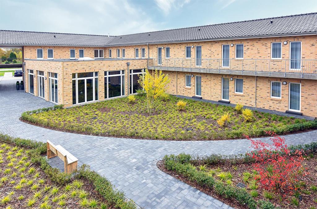 a large brick building with a garden in front of it at PRIMA Inn HOTEL & HOF NEURUPPIN - digitales & rezeptionsloses Motel in Neuruppin