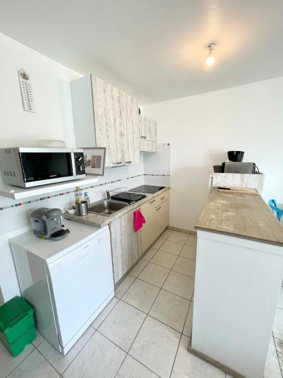 a white kitchen with a sink and a microwave at Charmant T2 À 50m de locéan in Ploemeur