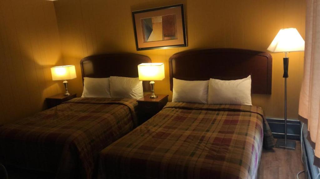 two beds in a hotel room with two lamps at Moose Motel in Smooth Rock Falls