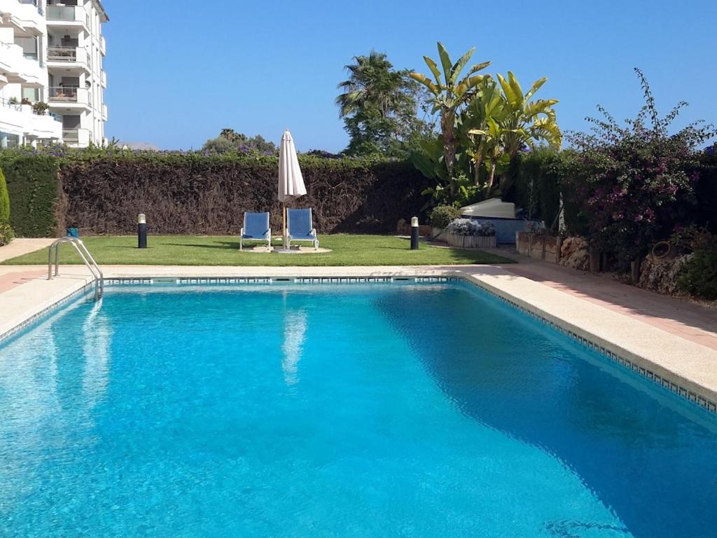 una piscina azul con sombrilla y 2 sillas en Belvilla by OYO Apartament Altea Mar, en Altea