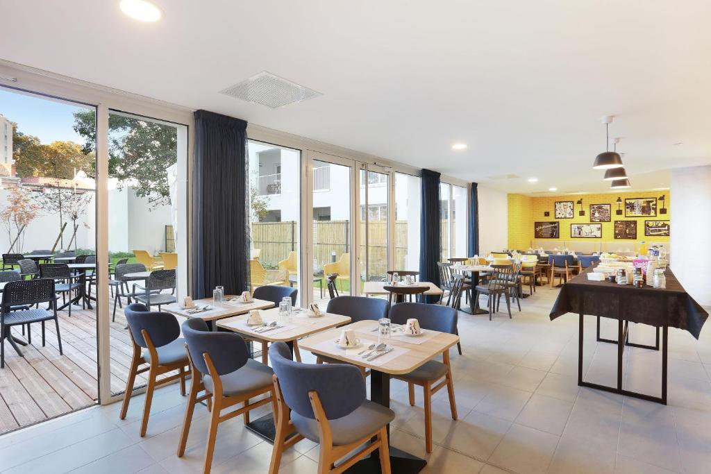 un comedor con mesas, sillas y ventanas en Appart Hotel Odalys City Toulouse Centre Compans Caffarelli, en Toulouse