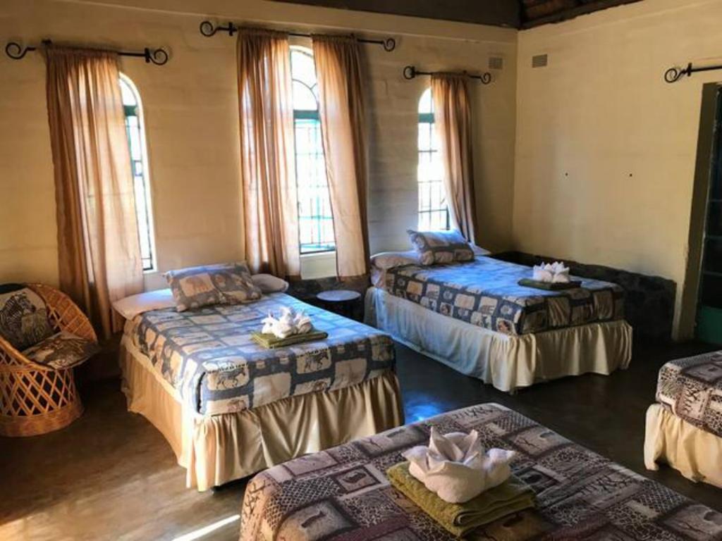 a room with three beds and windows at Bungalow 1 on this world renowned Eco site 40 minutes from Vic Falls Fully catered stay - 1978 in Victoria Falls