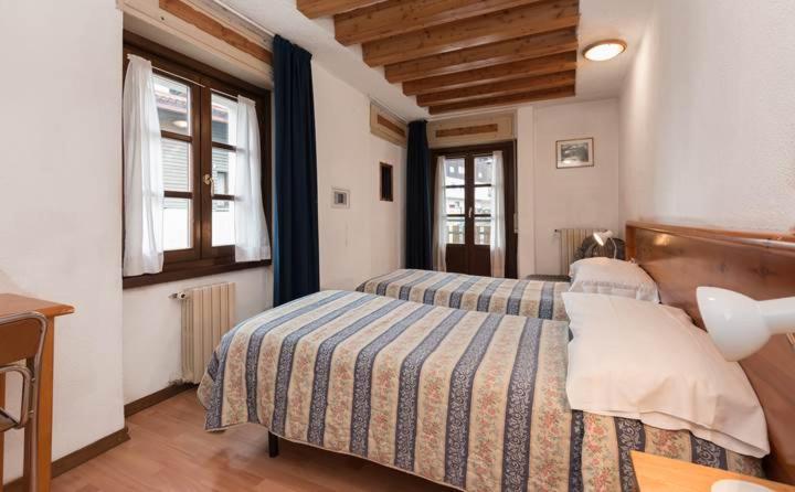 a bedroom with two beds and a table and two windows at Hotel Sport Cafe in Sauze dʼOulx